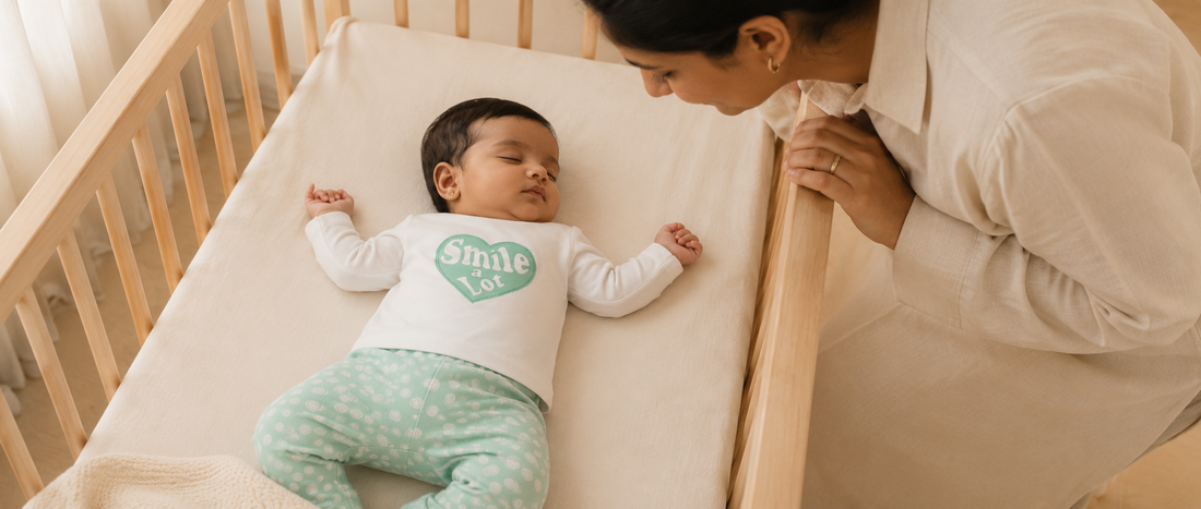Sleeping baby girl wearing a soft BabyRon Smile cotton pyjama set while her mother watches over her in a minimalist nursery, highlighting comfortable clothing for babies with sensitive skin